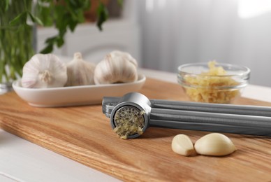 Photo of Garlic press with mince and cloves on wooden table indoors, closeup