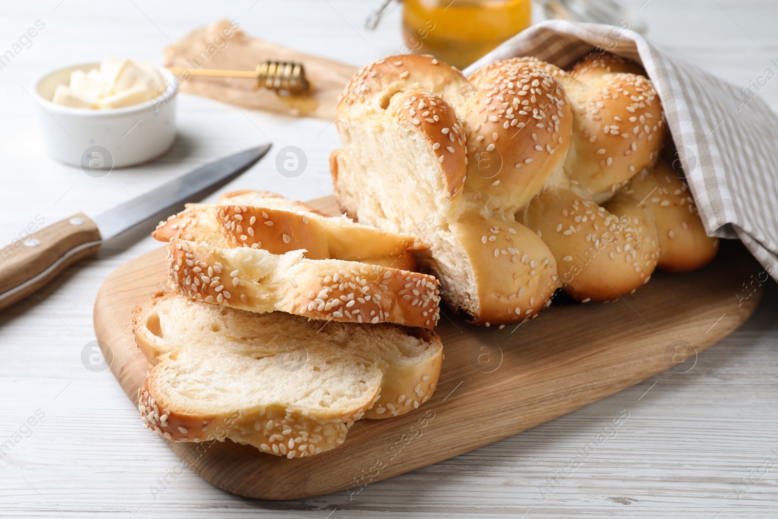 Photo of Cut freshly baked braided bread, knife and butter on white wooden table, closeup. Traditional Shabbat challah