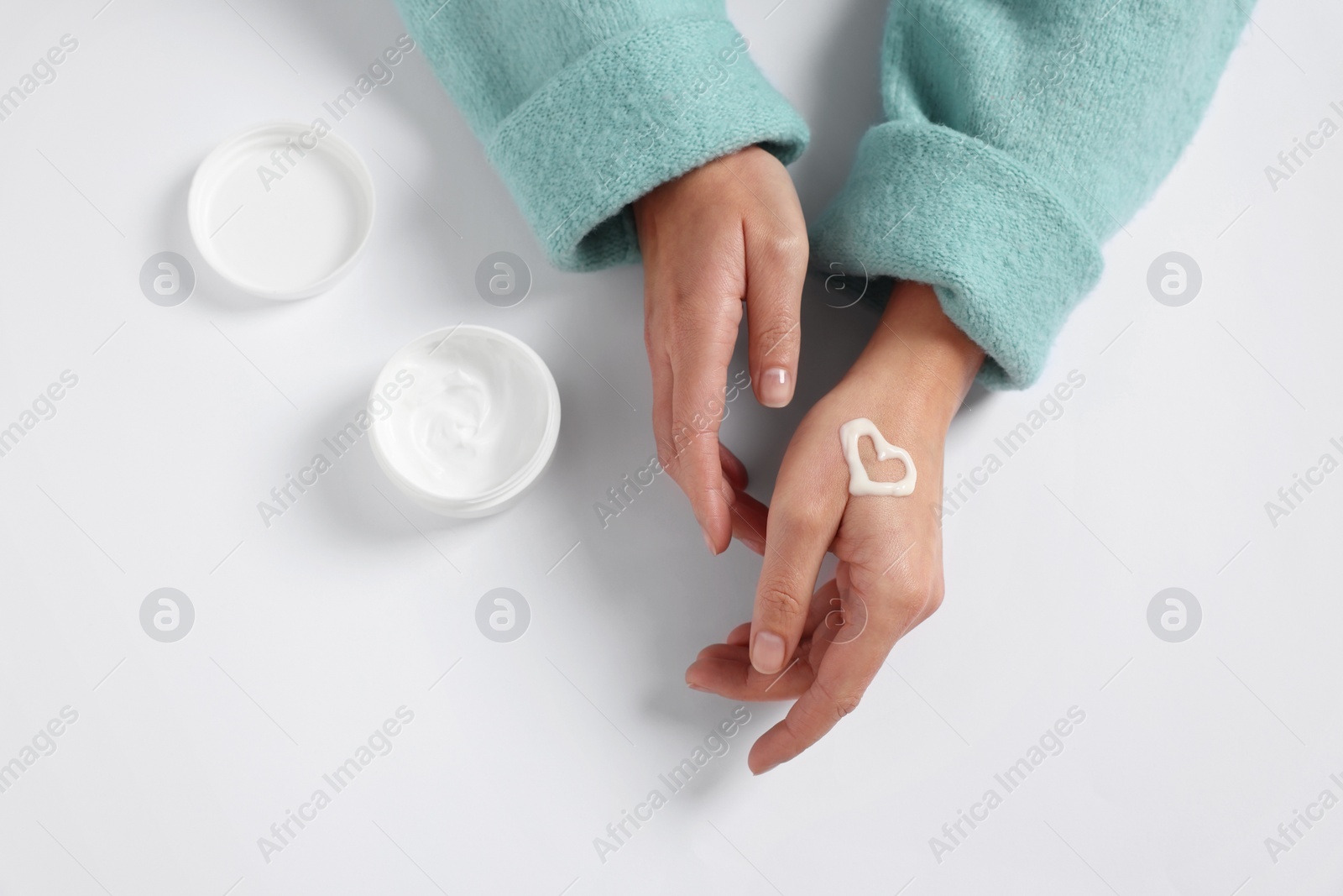 Photo of Woman with heart made of cosmetic cream on hand and jar against white background, top view