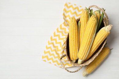 Photo of Basket of corn cobs on white wooden table, flat lay. Space for text