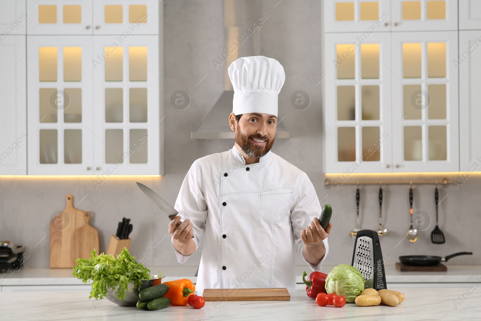 Photo of Portrait of chef with cucumber and knife at marble table in kitchen