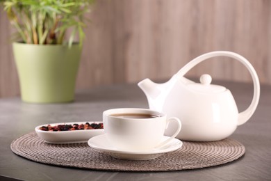 Photo of Aromatic tea in cup, saucer, teapot and dry flower petals on grey table