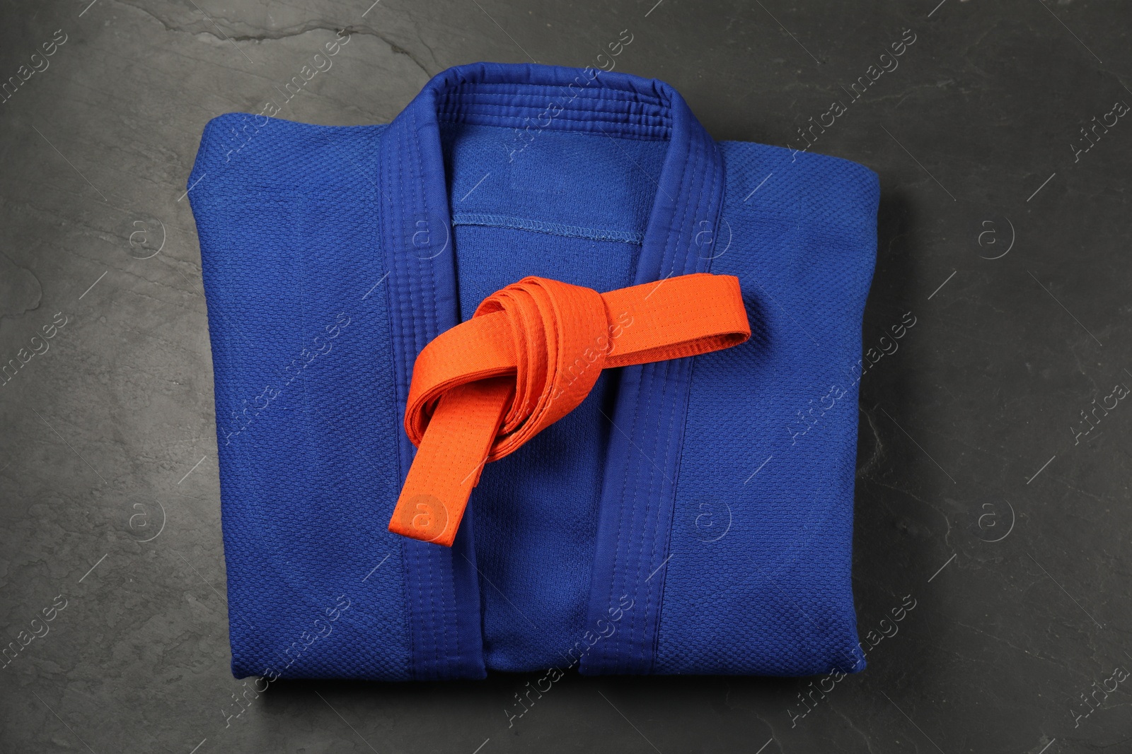 Photo of Orange karate belt and blue kimono on gray background, top view