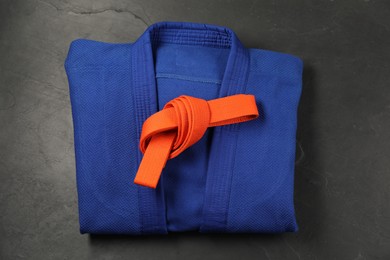 Photo of Orange karate belt and blue kimono on gray background, top view