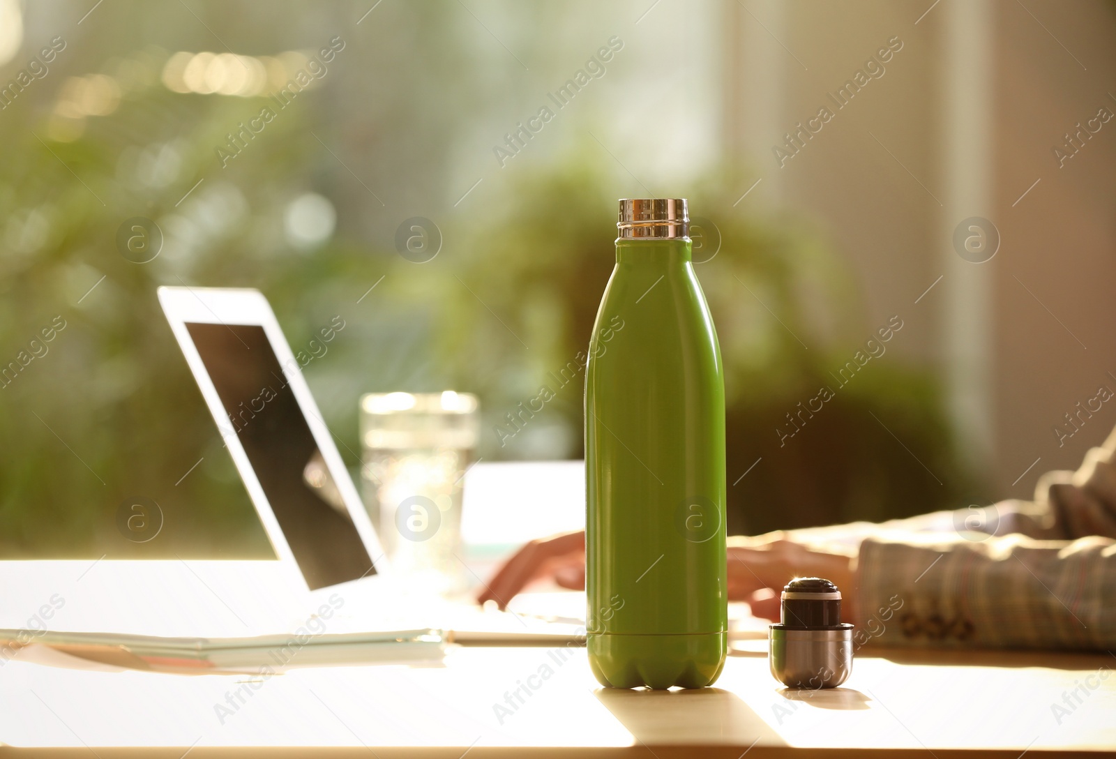 Photo of Woman working at table in modern office, focus on green thermos bottle. Space for text