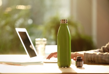 Woman working at table in modern office, focus on green thermos bottle. Space for text