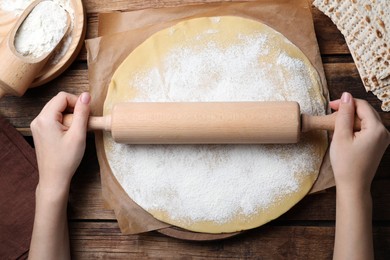 Photo of Woman rolling raw dough for traditional matzo at wooden table, top view
