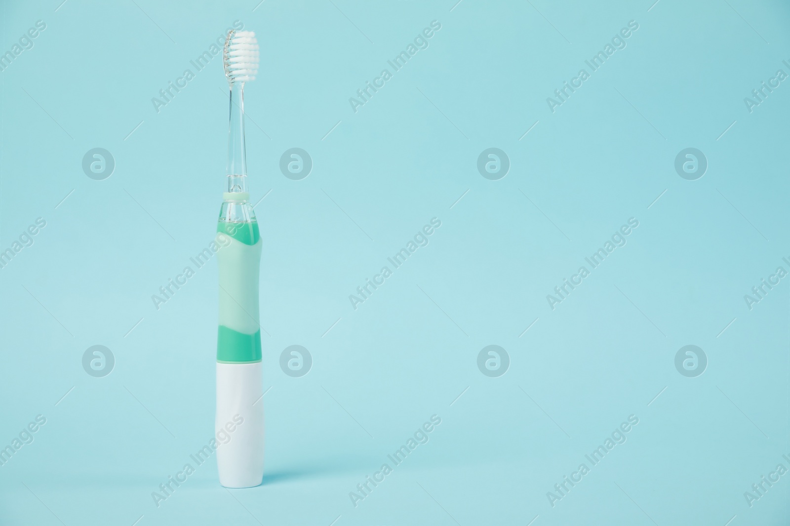 Photo of Electric toothbrush on light blue background, space for text