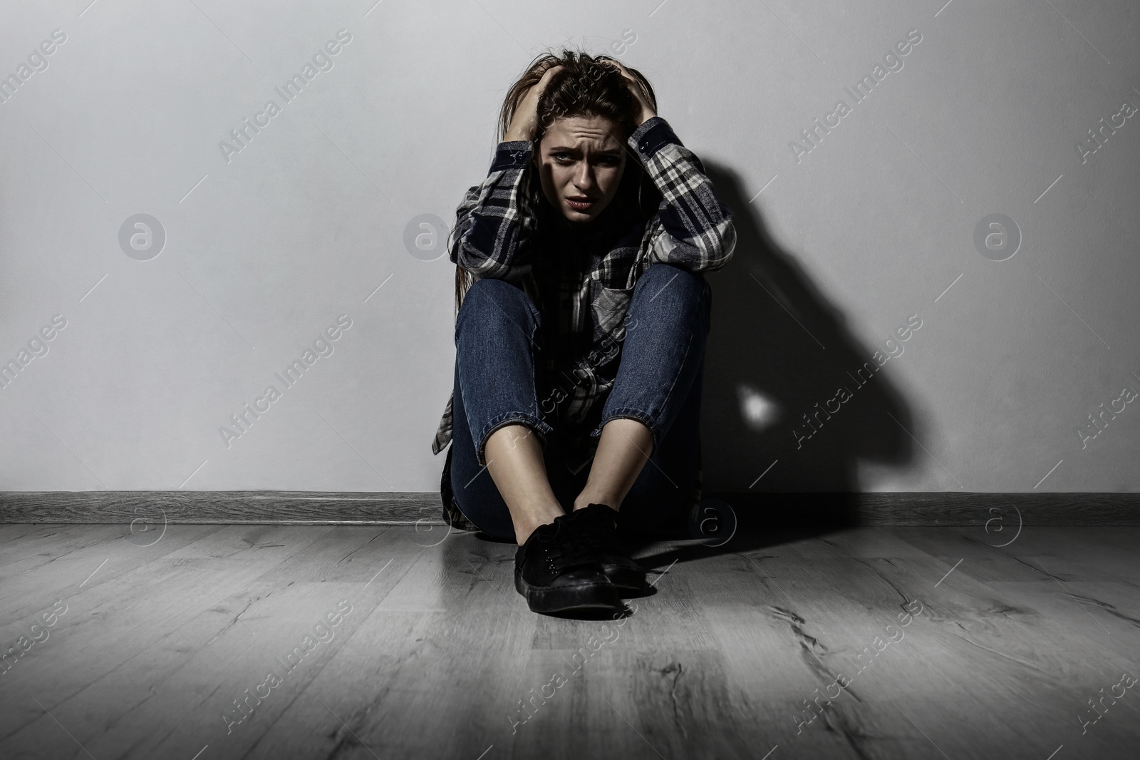 Image of Depressed young woman sitting alone near light wall. Autophobia - fear of isolation