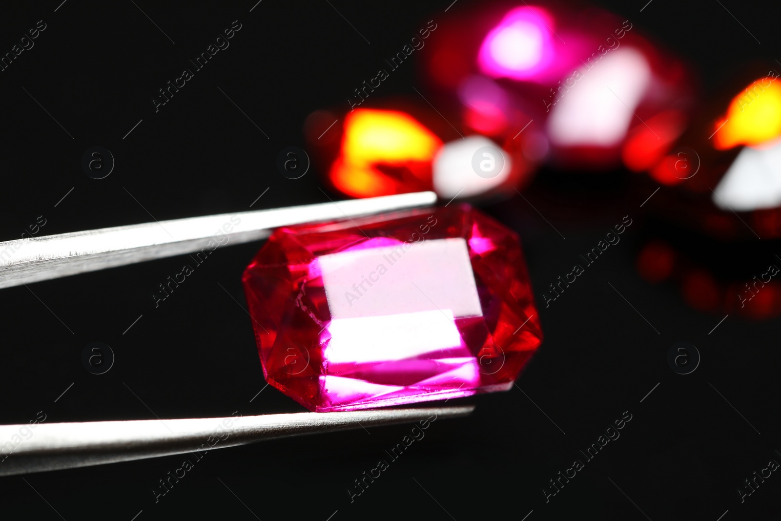 Photo of Tweezers with beautiful gemstone on dark background, closeup