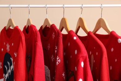 Rack with different Christmas sweaters on beige background, closeup