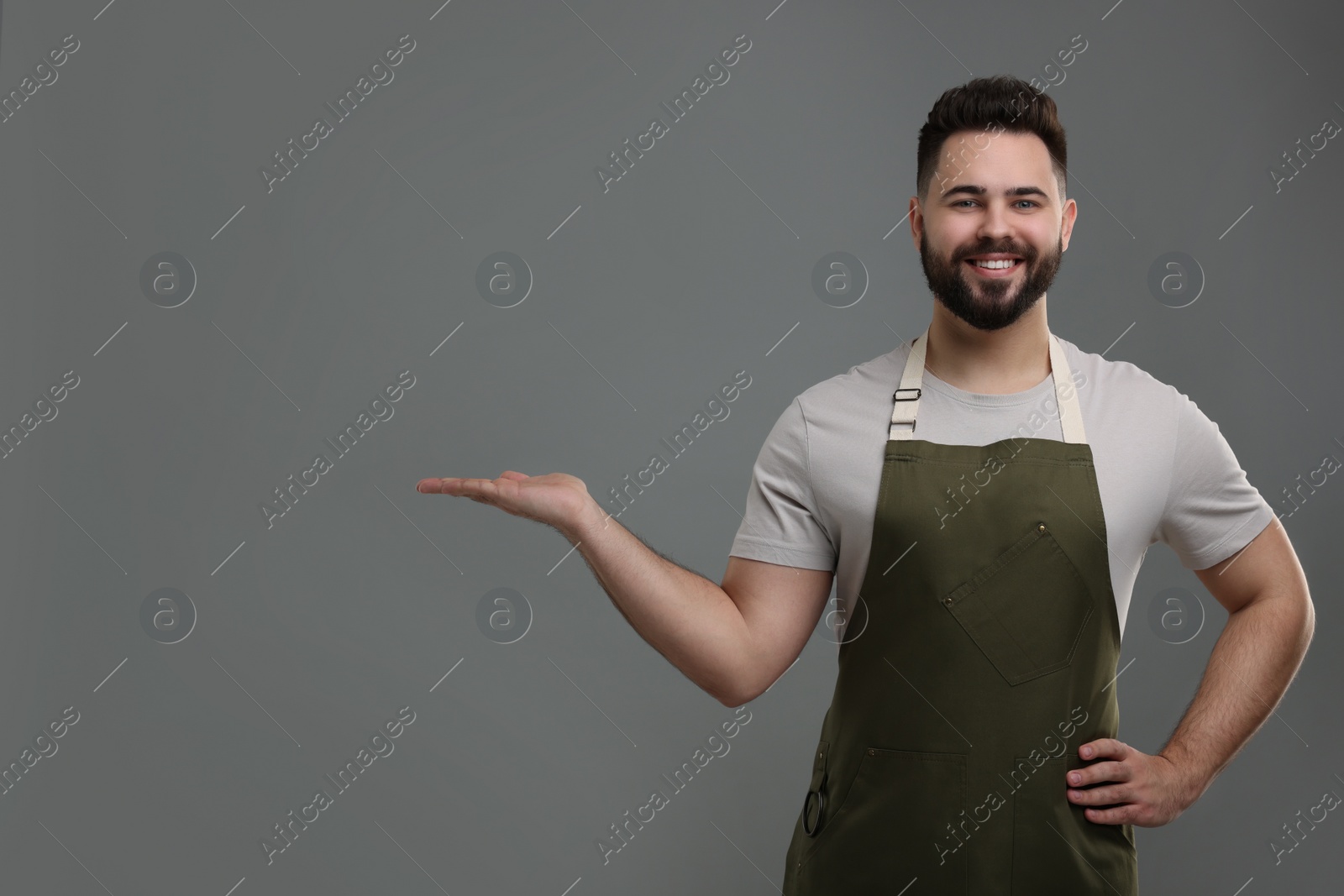 Photo of Smiling man in kitchen apron holding something on grey background. Mockup for design