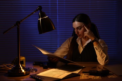 Professional detective working with documents in office at night