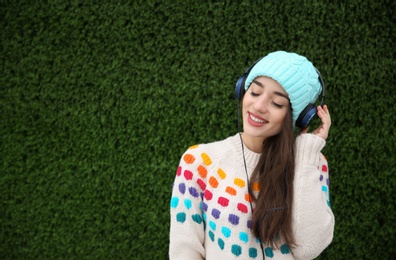 Photo of Beautiful young woman listening to music with headphones near grass wall. Space for text