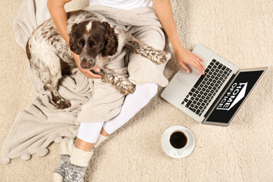 Image of Young woman with laptop and her dog on light carpet, top view. Home office