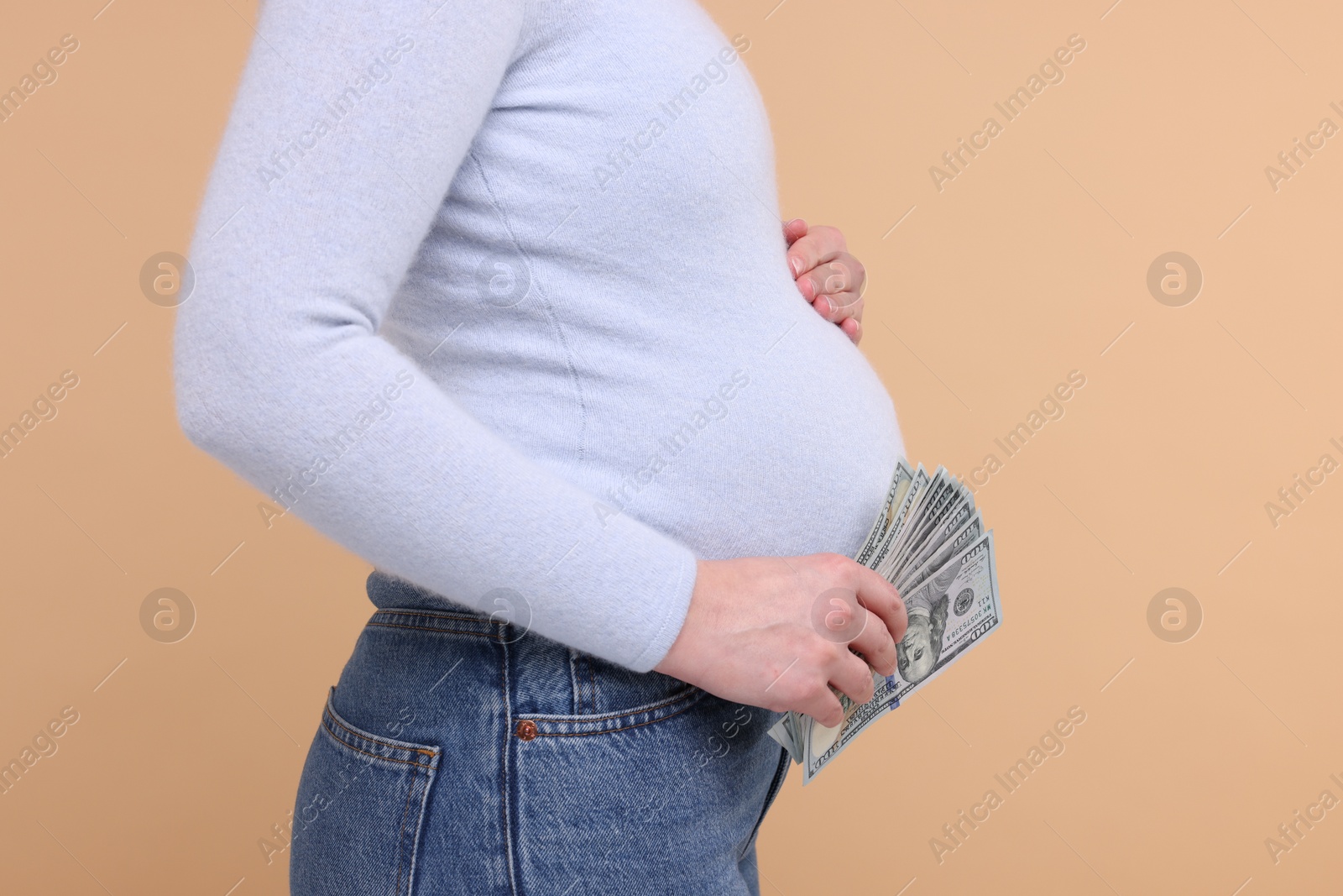 Photo of Surrogate mother. Pregnant woman with dollar banknotes on beige background, closeup