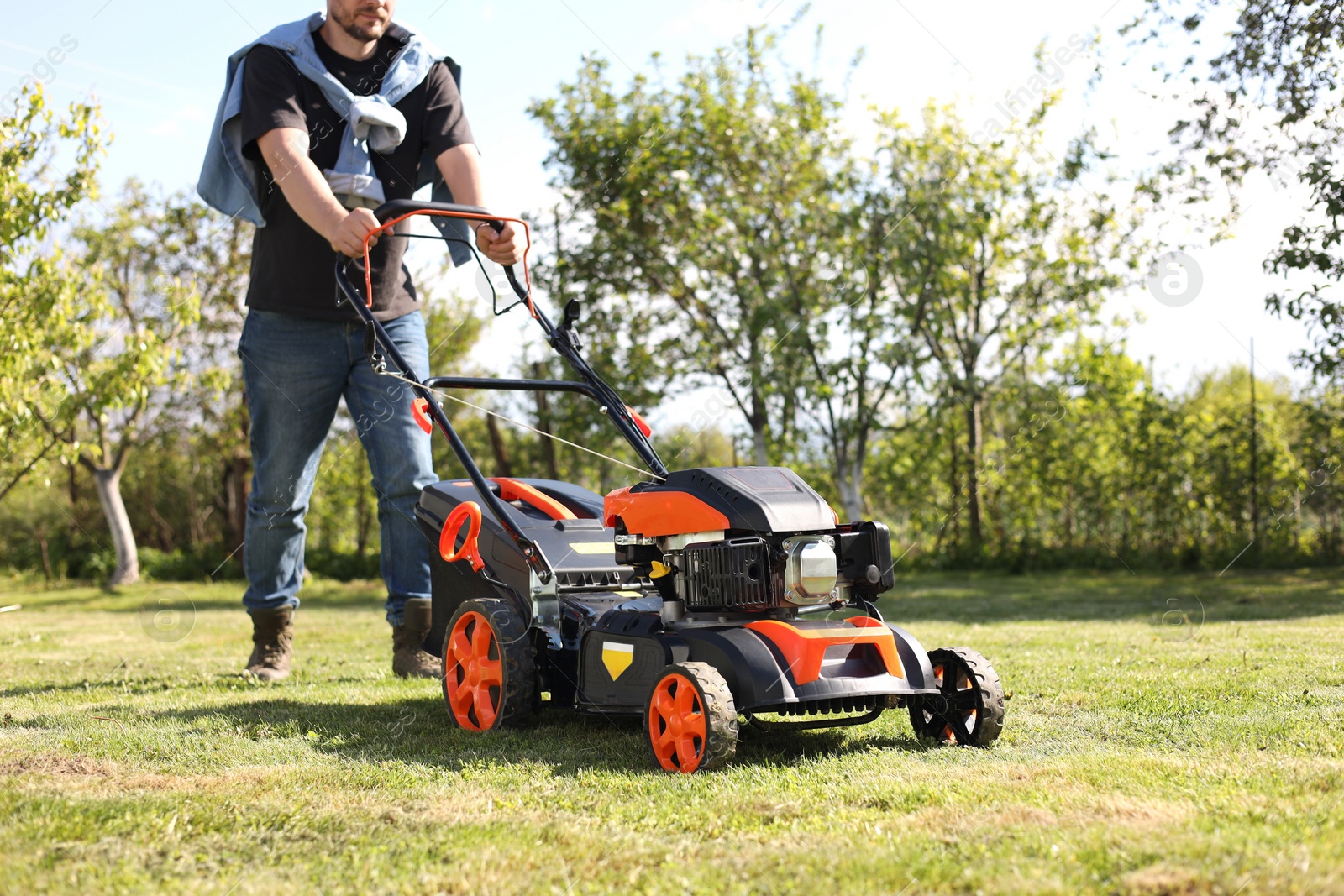 Photo of Man cutting green grass with lawn mower in garden, closeup