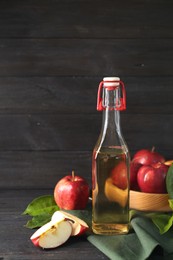 Photo of Bottle of delicious cider, cut and whole apples with green leaves on black wooden table