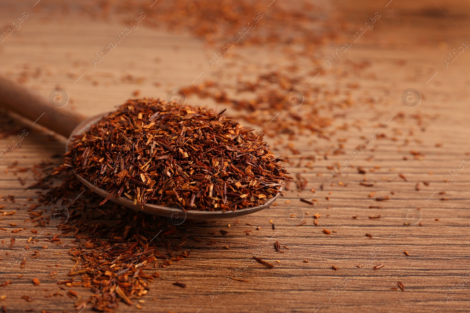 Photo of Spoon with dry rooibos leaves on wooden table, closeup. Space for text