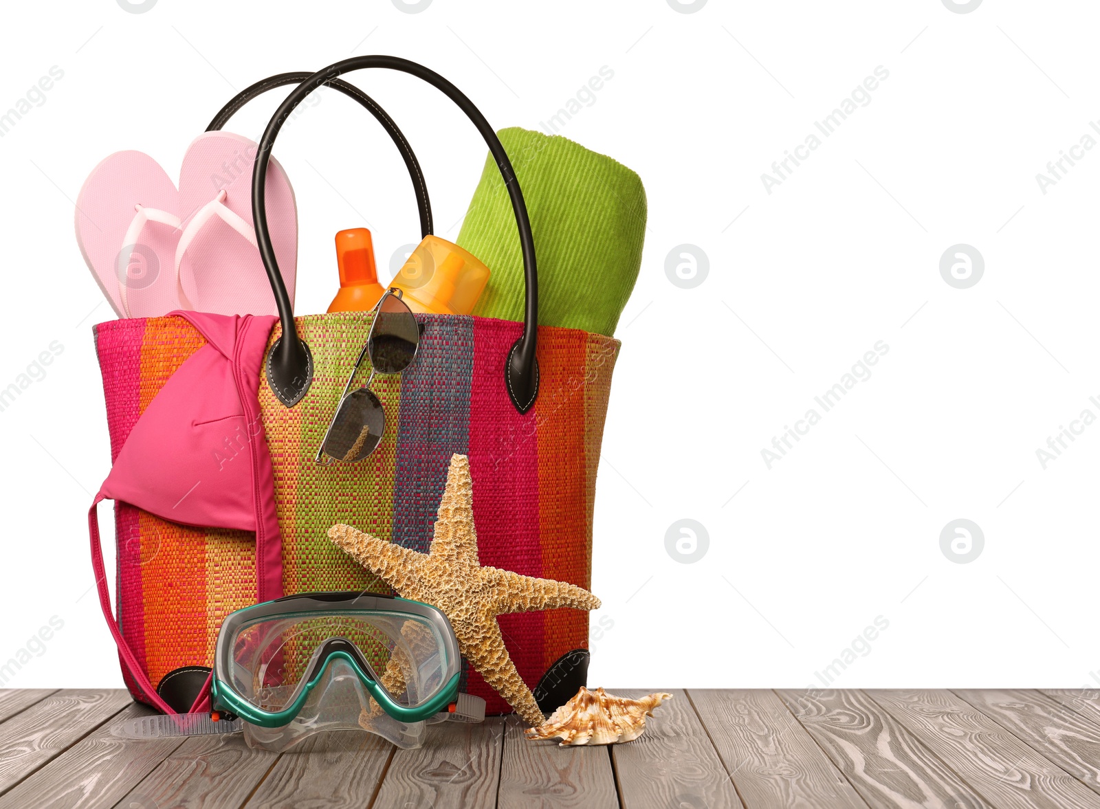 Photo of Stylish bag with beach accessories on wooden table against white background