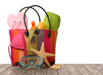 Stylish bag with beach accessories on wooden table against white background