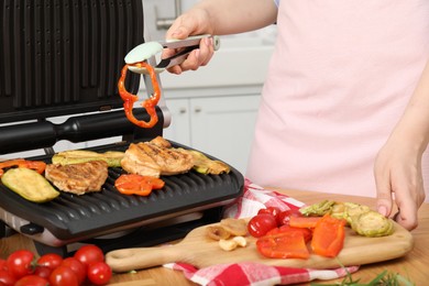 Woman cooking different products with electric grill at wooden table in kitchen, closeup