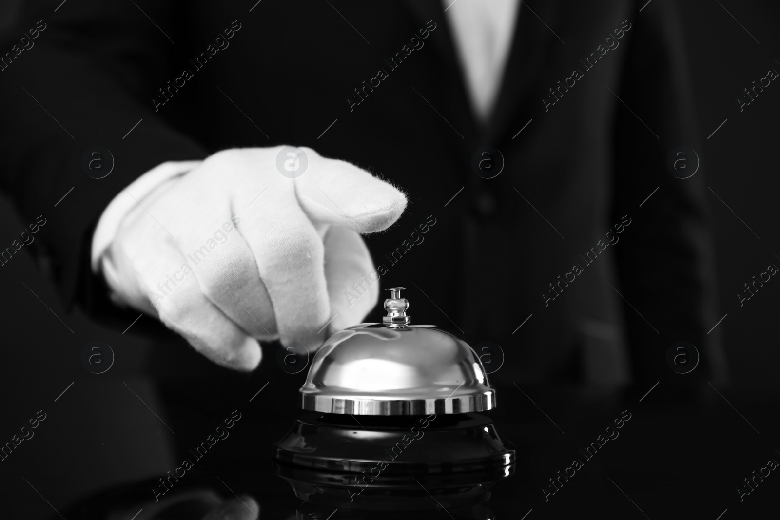 Photo of Butler ringing service bell at table on black background, closeup
