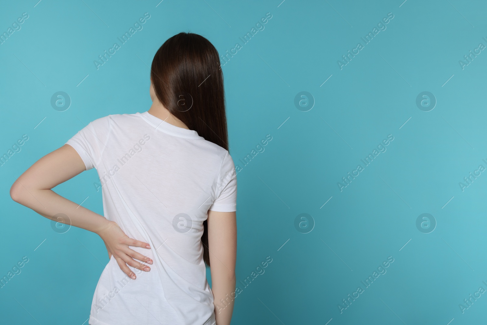 Photo of Woman suffering from back pain on light blue background, space for text. Arthritis symptoms
