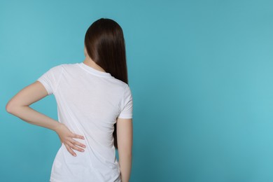 Woman suffering from back pain on light blue background, space for text. Arthritis symptoms