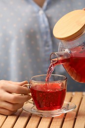 Woman pouring delicious hibiscus tea into cup at wooden table, closeup