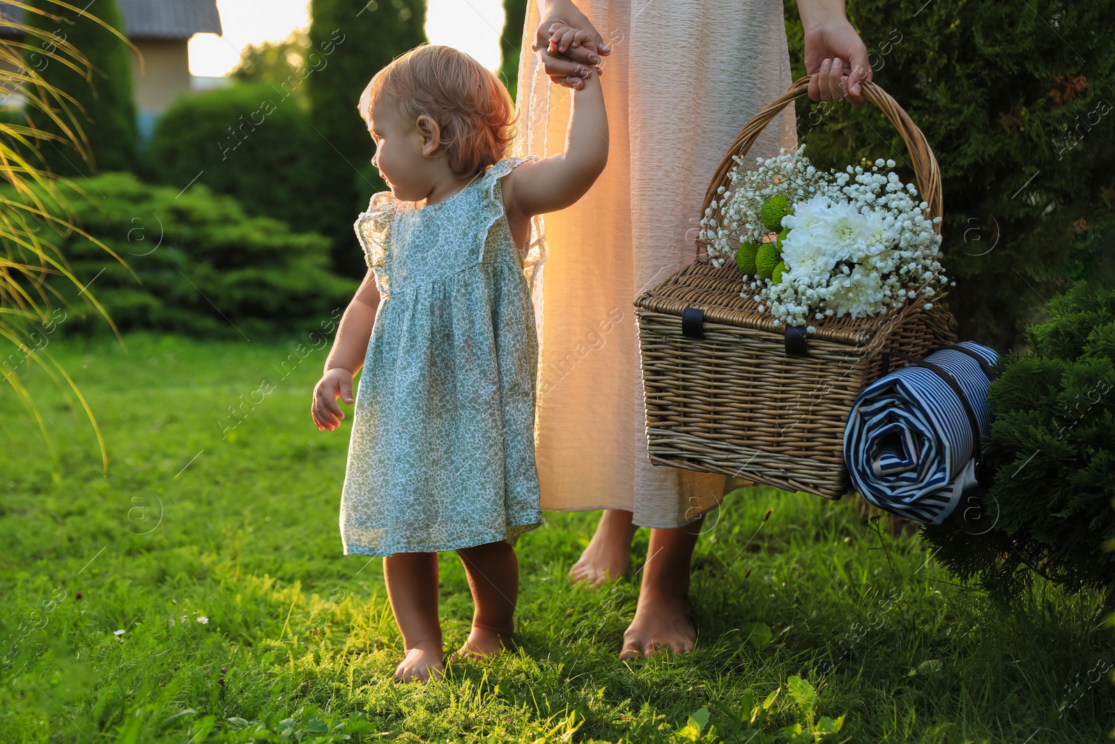 Photo of Adorable baby girl and her mother with picnic basket in garden on sunny day