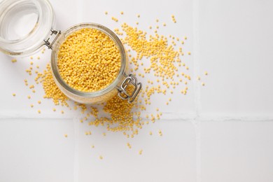 Photo of Millet groats in glass jar on white tiled table, top view. Space for text