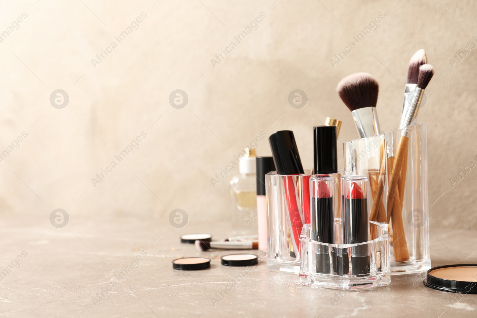 Photo of Lipstick holder with different makeup products on table against color background. Space for text