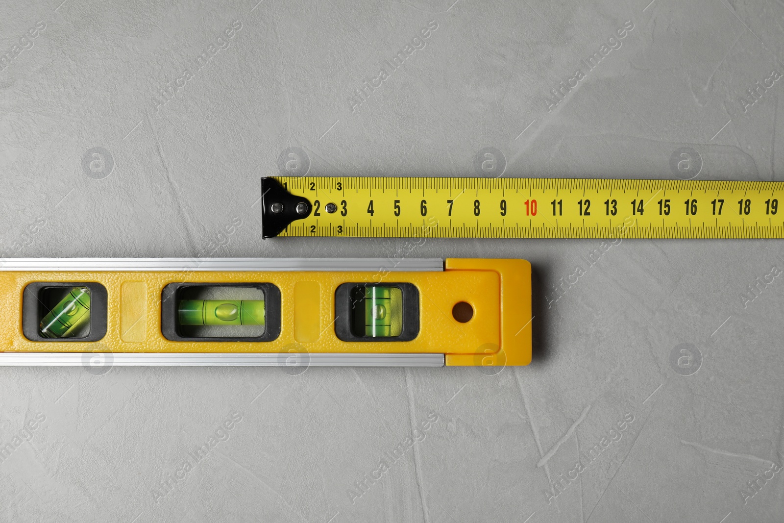 Photo of Building level and tape measure on grey table, top view