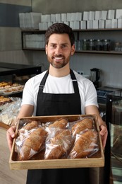 Photo of Happy seller holding tray with tasty croissants in bakery shop