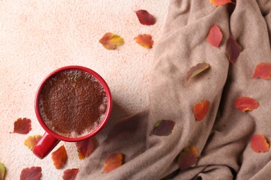 Photo of Cup of hot drink, leaves and soft knitted fabric on beige textured table, flat lay. Cozy autumn atmosphere