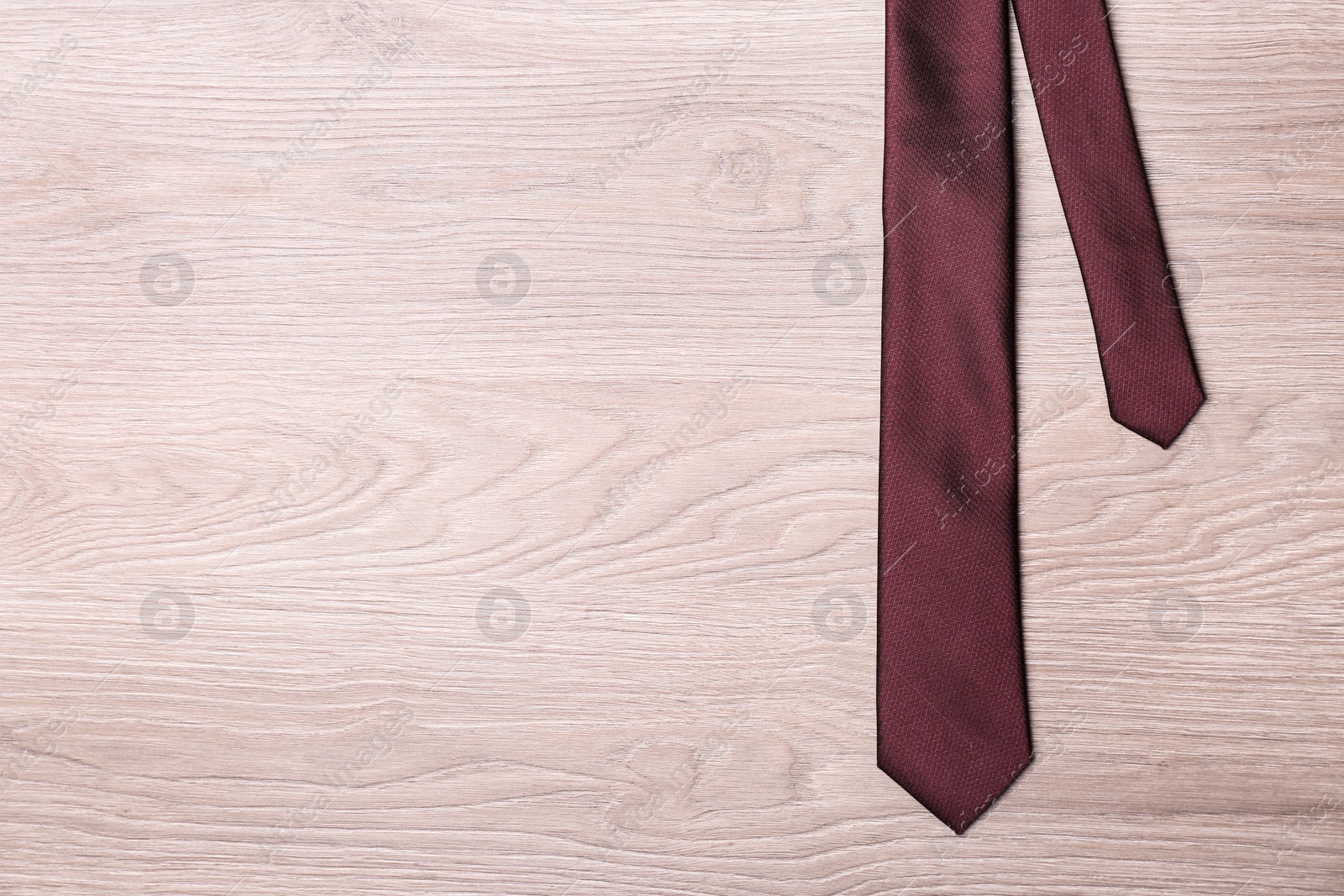 Photo of Stylish bordeaux necktie on wooden table, top view with space for text