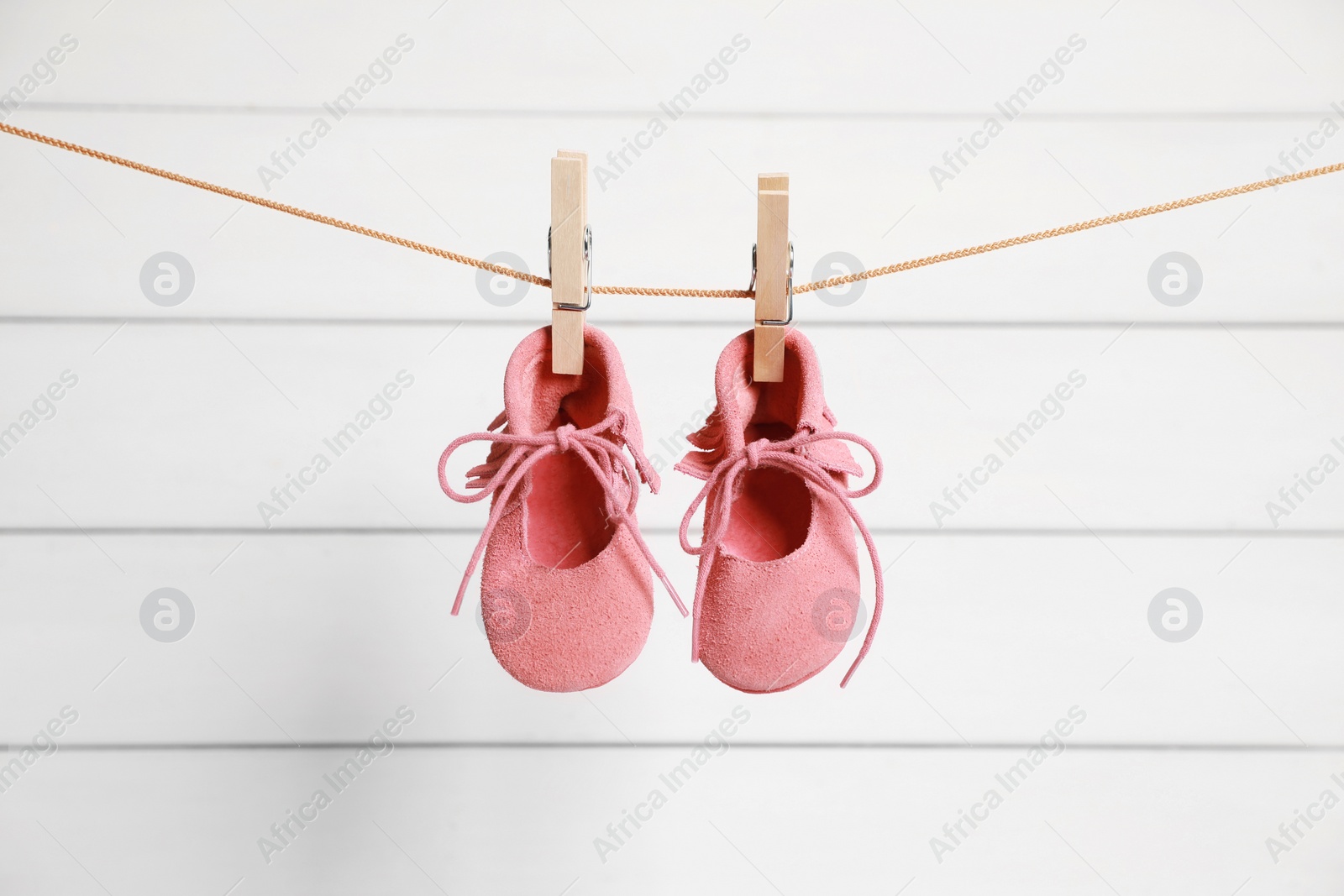 Photo of Pink baby shoes drying on washing line against white wall