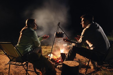 Photo of Couple near bonfire outdoors in evening. Camping season