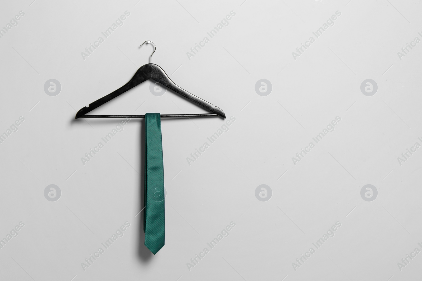 Photo of Hanger with green necktie on light grey wall. Space for text