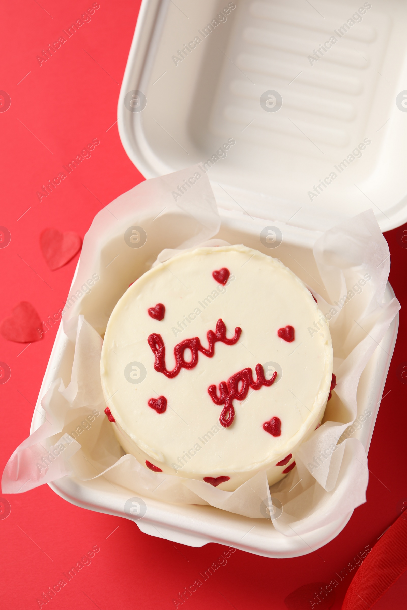 Photo of Bento cake with Love You text in takeaway box on red table, top view. St. Valentine's day surprise