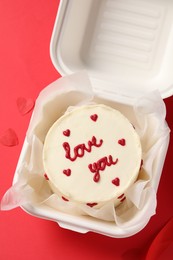 Bento cake with Love You text in takeaway box on red table, top view. St. Valentine's day surprise