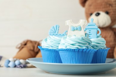 Photo of Beautifully decorated baby shower cupcakes with cream and boy toppers on white table. Space for text