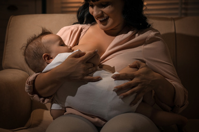 Woman breastfeeding her little baby on sofa in evening