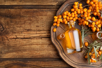 Photo of Natural sea buckthorn oil and fresh berries on wooden table, top view. Space for text