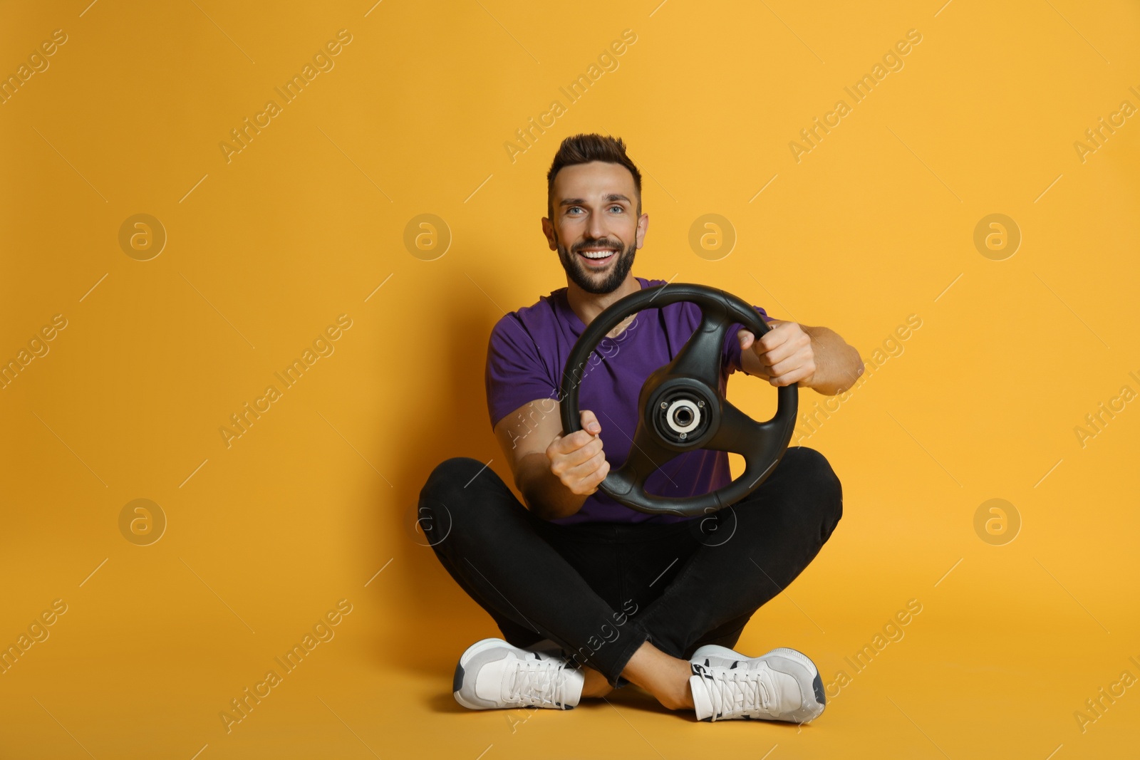 Photo of Happy man with steering wheel on yellow background