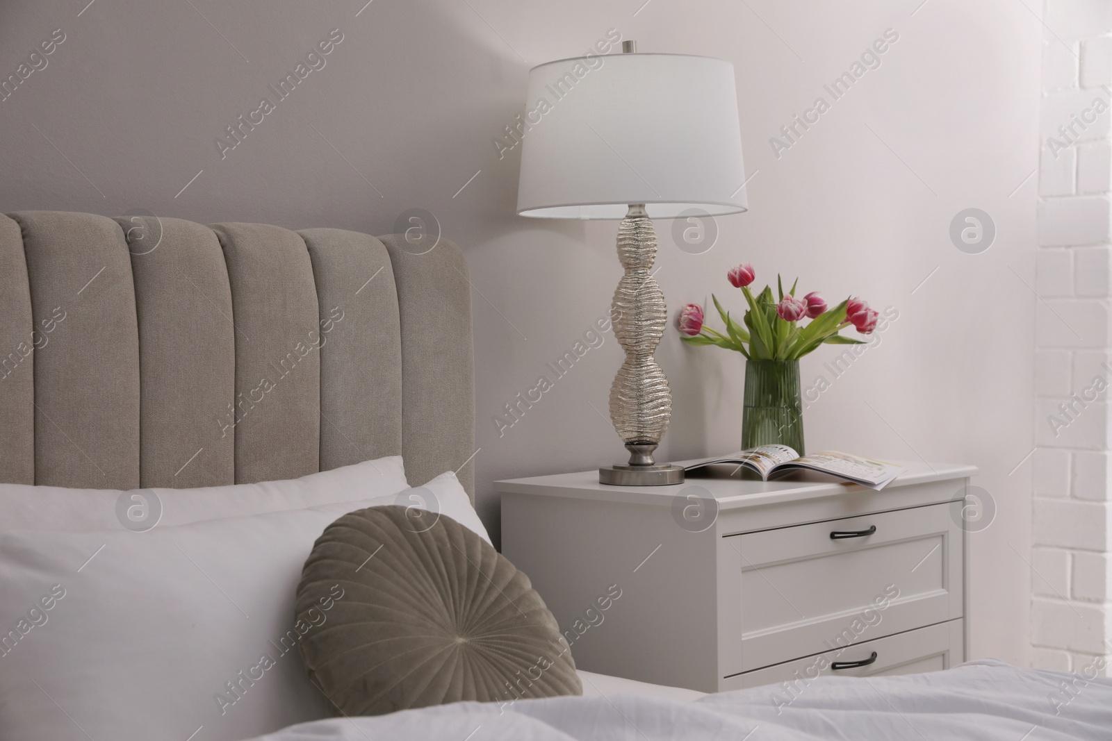 Photo of Stylish lamp, flowers and magazine on bedside table indoors. Bedroom interior elements