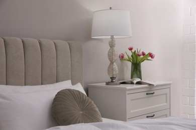 Stylish lamp, flowers and magazine on bedside table indoors. Bedroom interior elements