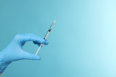 Photo of Doctor holding syringe on light blue background, closeup. Space for text