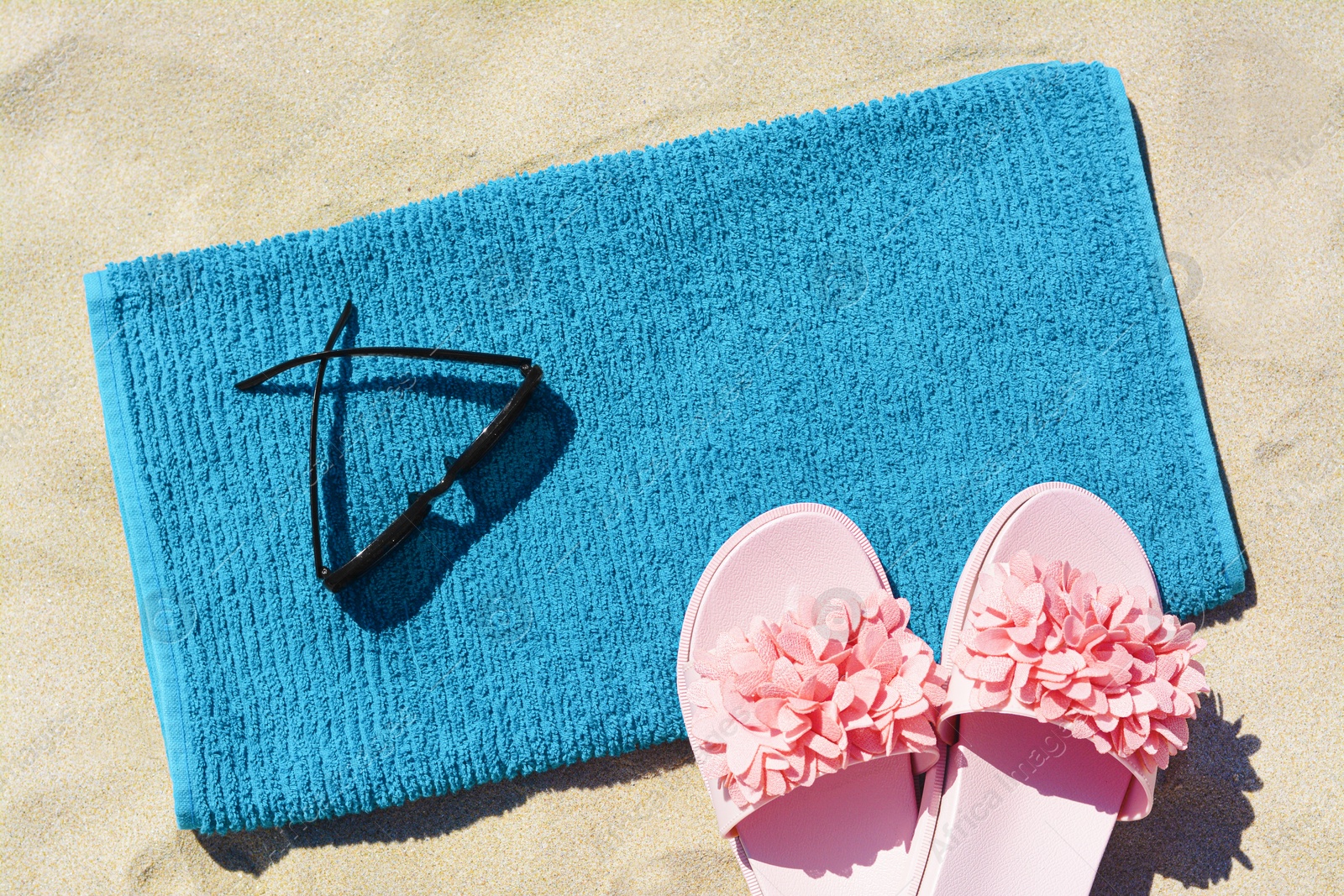Photo of Towel, flip flops and sunglasses on sand, flat lay. Beach accessories